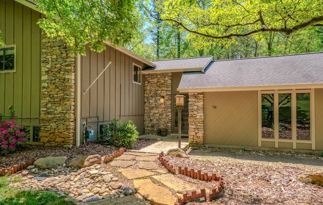 doorway to property with board and batten siding, stone siding, and roof with shingles