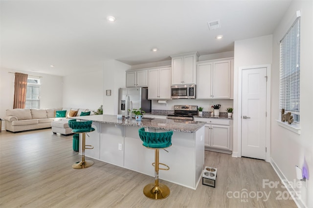 kitchen with open floor plan, stainless steel appliances, an island with sink, and a kitchen breakfast bar