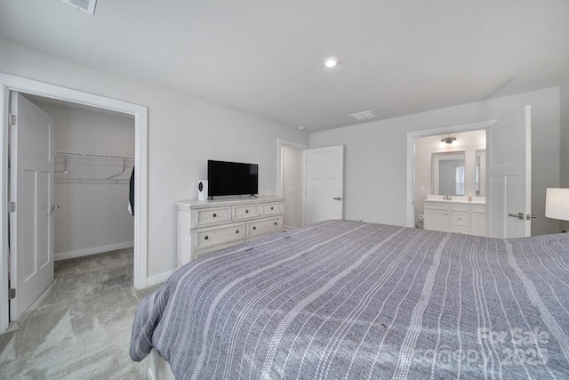 bedroom with ensuite bathroom, a spacious closet, light carpet, and a closet