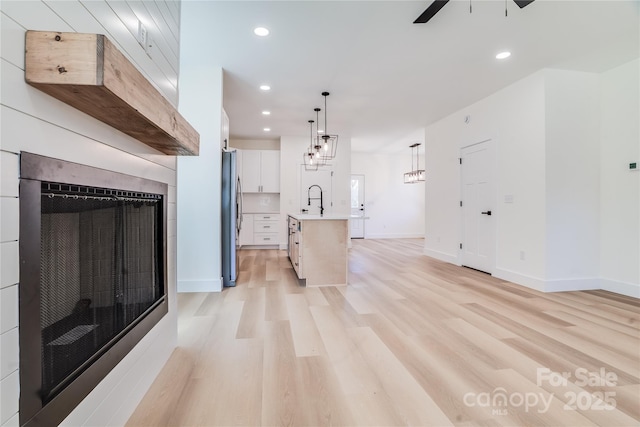 kitchen with freestanding refrigerator, light countertops, a sink, and light wood finished floors