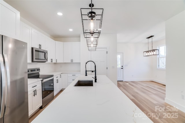 kitchen featuring light wood-style flooring, appliances with stainless steel finishes, white cabinetry, a sink, and light stone countertops