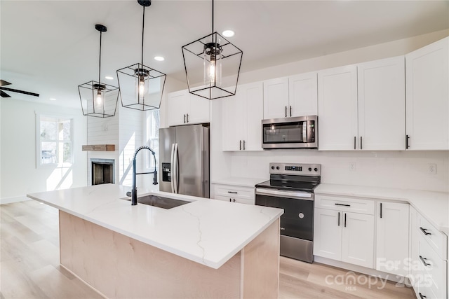 kitchen with light wood finished floors, appliances with stainless steel finishes, light stone countertops, a fireplace, and a sink