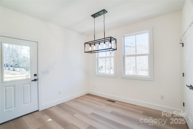 unfurnished dining area with light wood-type flooring, an inviting chandelier, baseboards, and visible vents