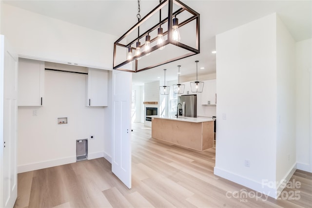 kitchen with light wood finished floors, light countertops, a glass covered fireplace, white cabinetry, and stainless steel fridge with ice dispenser