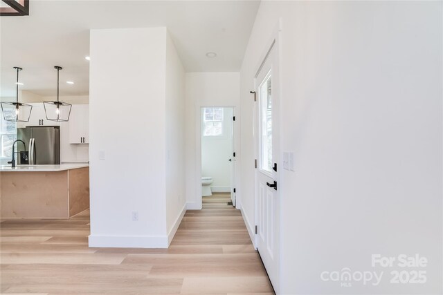 hallway with light wood-style floors, baseboards, a sink, and recessed lighting