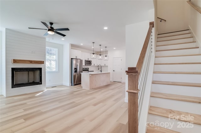 interior space featuring recessed lighting, light wood-style floors, a ceiling fan, a large fireplace, and a sink