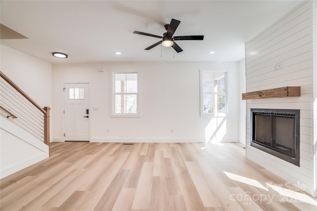 unfurnished living room featuring a wealth of natural light, a large fireplace, light wood-style flooring, and stairs