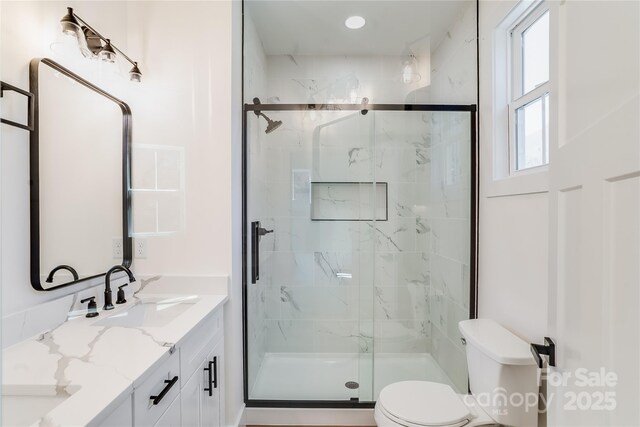 full bathroom featuring a marble finish shower, double vanity, a sink, and toilet