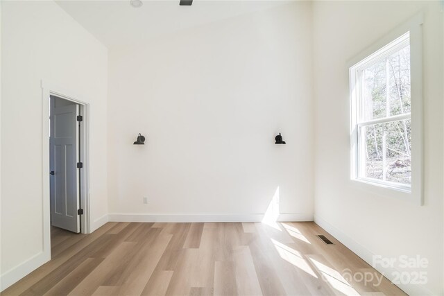 spare room with light wood-type flooring, visible vents, and baseboards