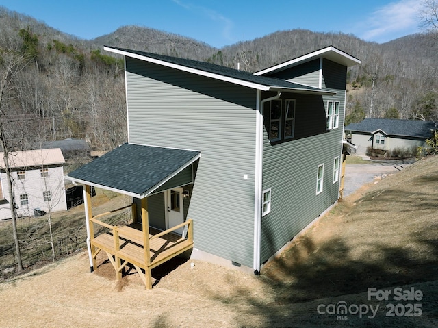 view of side of property featuring crawl space, roof with shingles, a mountain view, and a wooded view