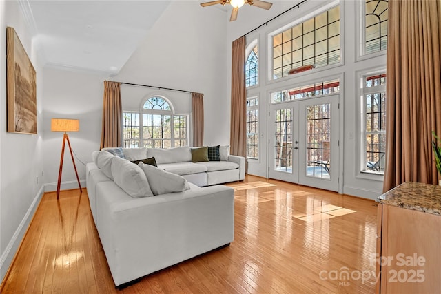 living room with a towering ceiling, light hardwood / wood-style flooring, french doors, and a healthy amount of sunlight