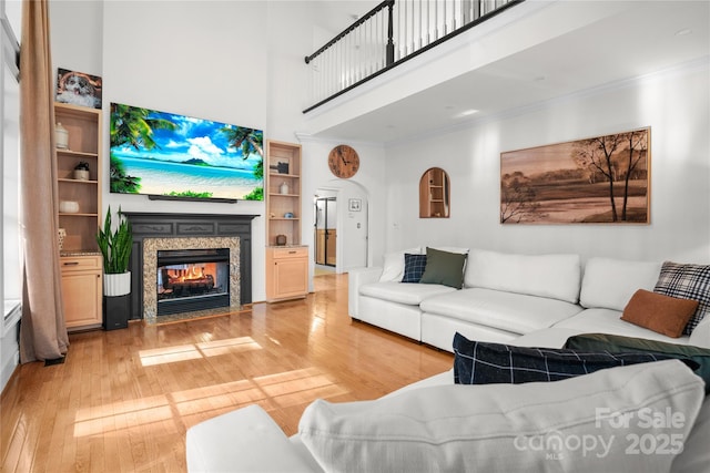 living room featuring a multi sided fireplace, ornamental molding, a towering ceiling, and light wood-type flooring