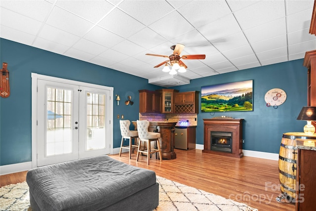 living room featuring ceiling fan, a drop ceiling, light wood-type flooring, and french doors