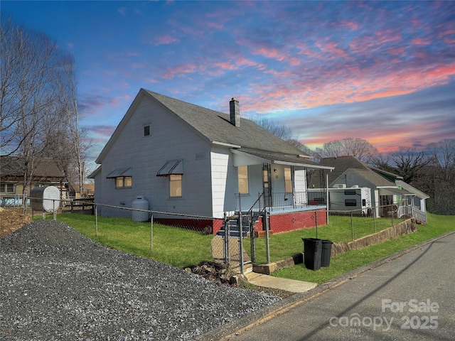 view of front facade featuring roof with shingles, a fenced front yard, a chimney, and a yard