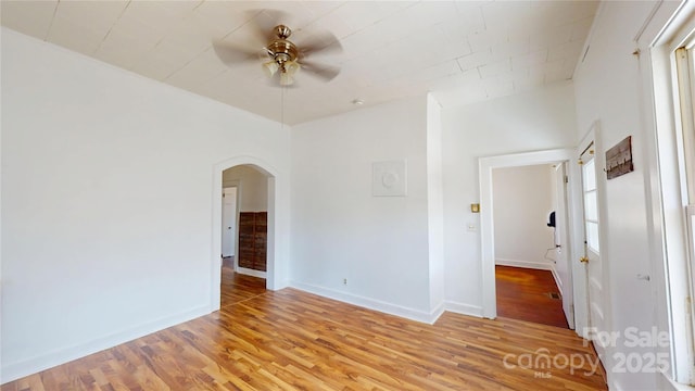 spare room featuring light wood-style flooring, baseboards, and arched walkways