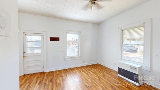 interior space with light wood-type flooring, ceiling fan, baseboards, and a wall mounted AC