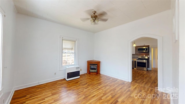 unfurnished room with heating unit, ceiling fan, arched walkways, wood finished floors, and baseboards