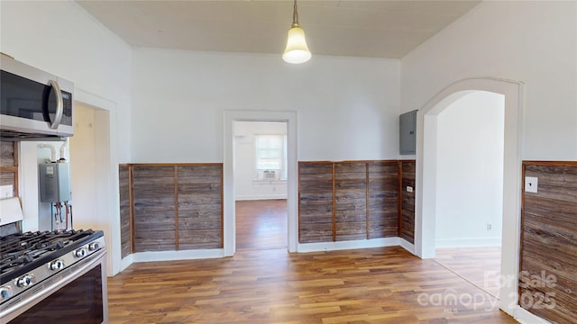 kitchen with wainscoting, electric panel, stainless steel appliances, arched walkways, and wood finished floors