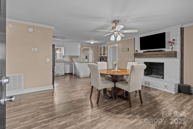 dining room with hardwood / wood-style flooring, ornamental molding, a brick fireplace, and ceiling fan