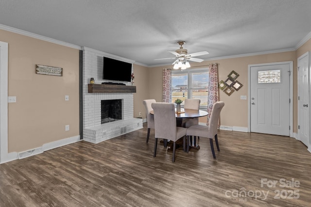 dining space featuring crown molding, a brick fireplace, a textured ceiling, dark hardwood / wood-style flooring, and ceiling fan