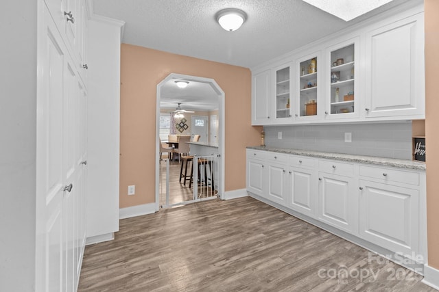 kitchen featuring backsplash, light hardwood / wood-style flooring, light stone countertops, and white cabinets