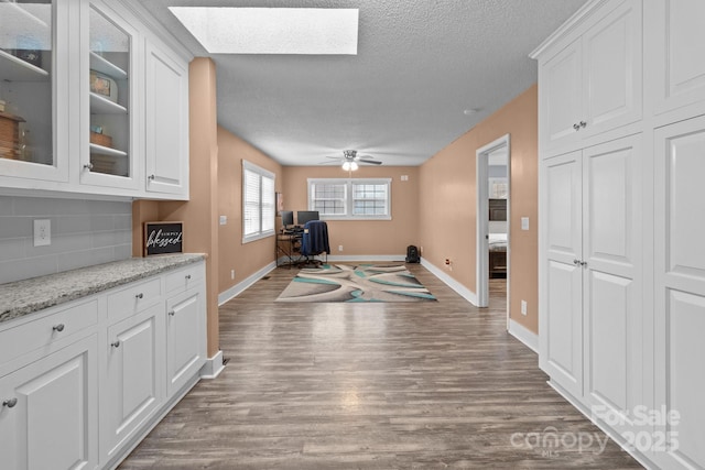 interior space with white cabinetry, wood-type flooring, light stone counters, and a skylight