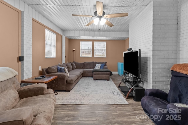 living room with hardwood / wood-style flooring, ceiling fan, and brick wall