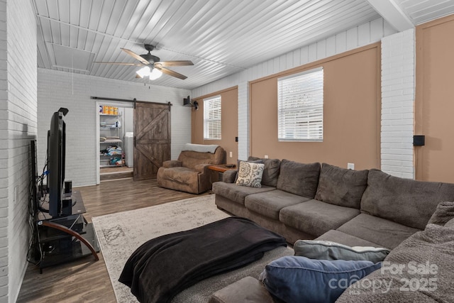 living room featuring a barn door, wood-type flooring, brick wall, and ceiling fan