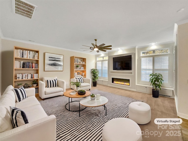 living room featuring ceiling fan, crown molding, built in shelves, and a baseboard heating unit