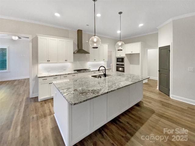 kitchen with a center island with sink, light stone countertops, sink, white cabinets, and wall chimney exhaust hood