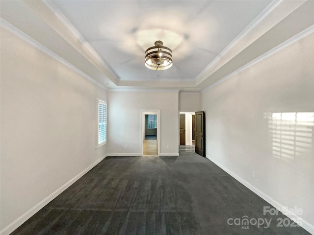 empty room with a tray ceiling, dark colored carpet, and ornamental molding