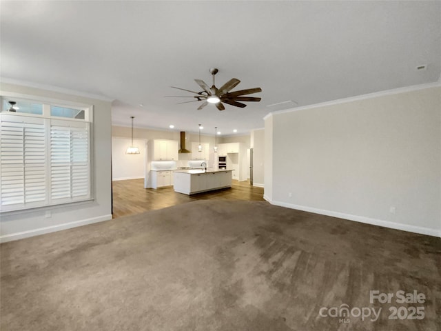 unfurnished living room with sink, ornamental molding, dark colored carpet, and ceiling fan