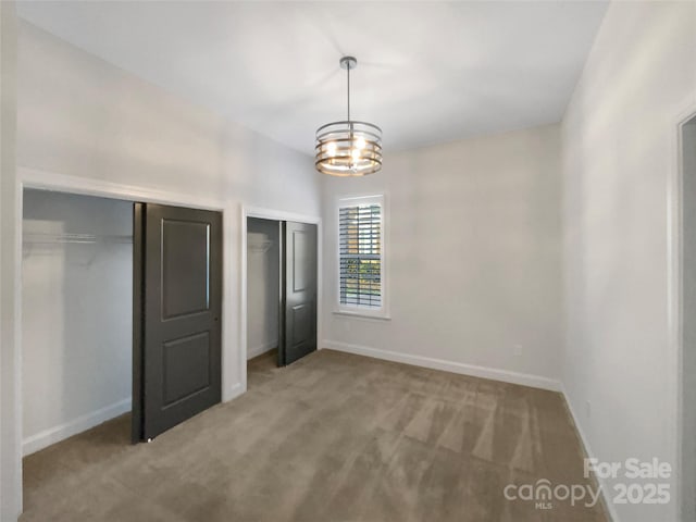 unfurnished bedroom featuring carpet, multiple closets, and a notable chandelier