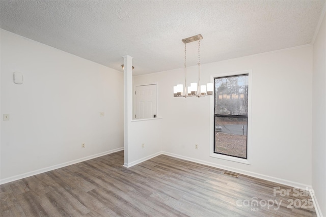 unfurnished dining area featuring an inviting chandelier, a textured ceiling, and hardwood / wood-style floors