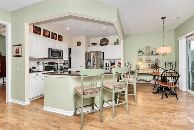 9119 Gander Dr, Charlotte, NC 28277 - kitchen with appliances with stainless steel finishes, decorative light fixtures, white cabinetry, a center island, and light hardwood / wood-style floors