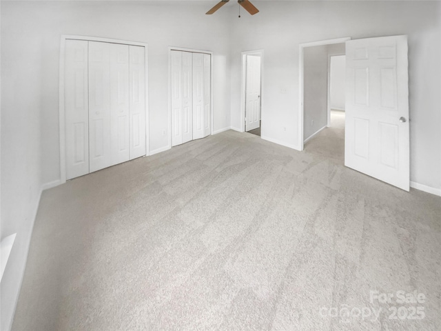 unfurnished bedroom featuring multiple closets, light colored carpet, and ceiling fan