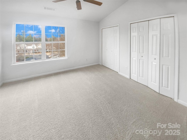 unfurnished bedroom with ceiling fan, carpet floors, multiple closets, and vaulted ceiling