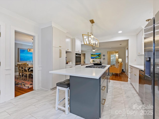 kitchen featuring a kitchen island, white cabinetry, hanging light fixtures, ornamental molding, and stainless steel appliances