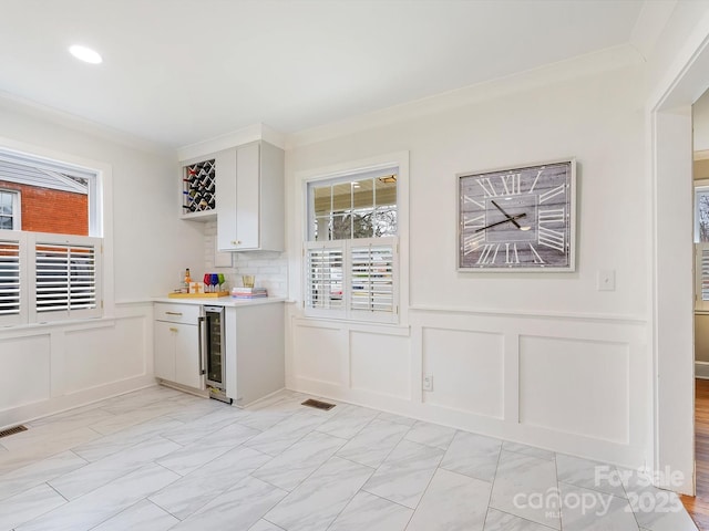 bar with white cabinetry, wine cooler, crown molding, and decorative backsplash