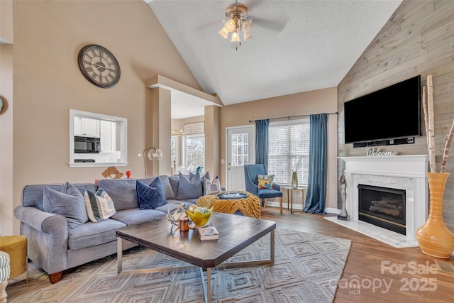 living area with a textured ceiling, high vaulted ceiling, a high end fireplace, a ceiling fan, and light wood-type flooring