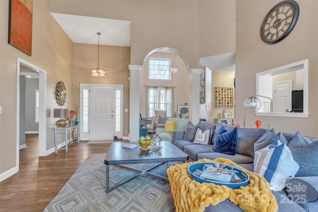 living room with arched walkways, baseboards, a high ceiling, dark wood-type flooring, and ornate columns