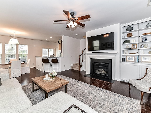 living room featuring dark wood-type flooring, ceiling fan, and built in shelves