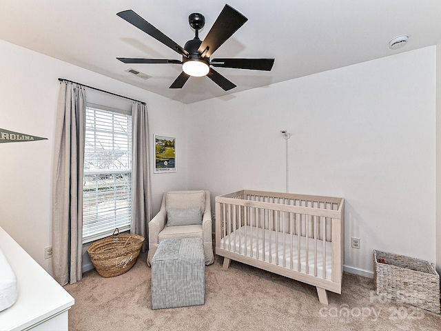 carpeted bedroom featuring a crib and ceiling fan