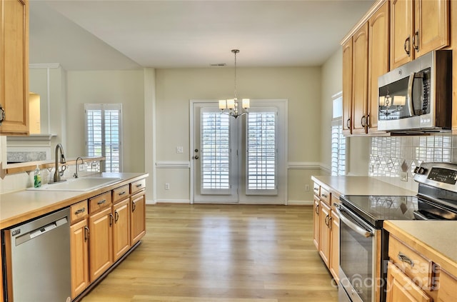 kitchen featuring tasteful backsplash, light wood-style flooring, appliances with stainless steel finishes, light countertops, and a sink