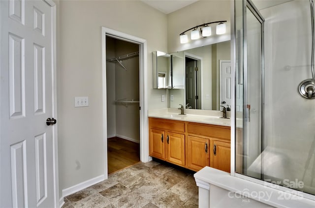 full bathroom with double vanity, a stall shower, baseboards, and a sink