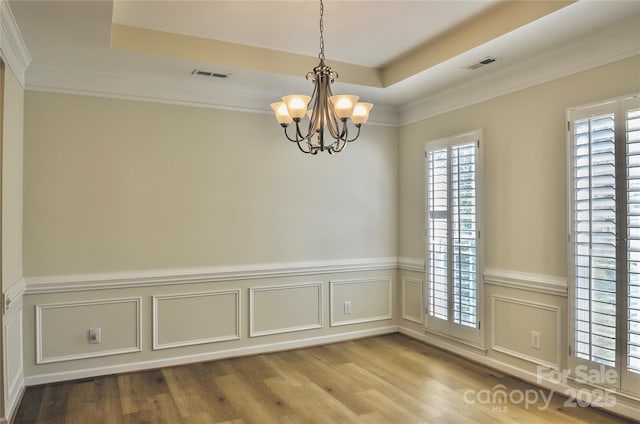 spare room with visible vents, a raised ceiling, wood finished floors, and a chandelier