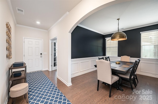 dining space with dark wood-type flooring, arched walkways, wainscoting, and ornamental molding