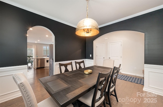 dining area featuring arched walkways, ornamental molding, a wainscoted wall, and wood finished floors