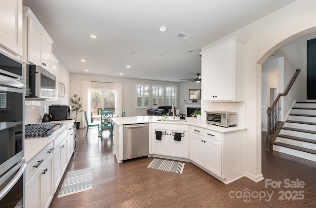 kitchen with stainless steel appliances, light countertops, open floor plan, white cabinets, and a sink