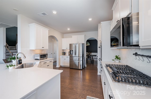 kitchen with arched walkways, stainless steel appliances, light countertops, visible vents, and white cabinetry